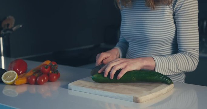 Young woman cutting a cucumber in kitchen