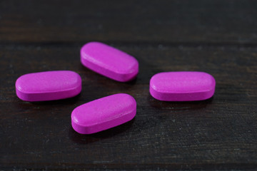 Pink Pharmaceutical medicine pills, tablets and capsules on a wooden background.