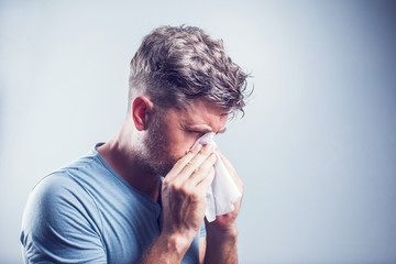 Man sneezing in a tissue outdoors. Pollen allergy, Springtime. - obrazy, fototapety, plakaty