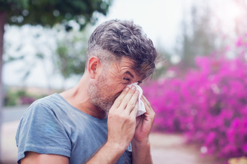Man sneezing in a tissue outdoors. Pollen allergy, Springtime. - obrazy, fototapety, plakaty