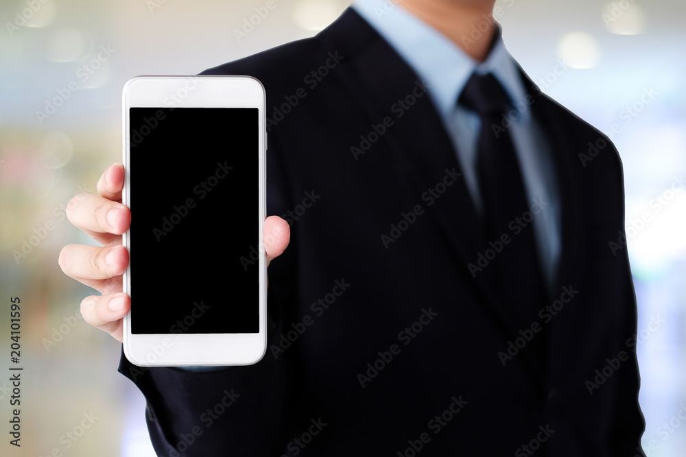 Wall mural Businessman hand holding smartphone with blank on screen display over blur background, business people and technology display montage, mock up, template, background