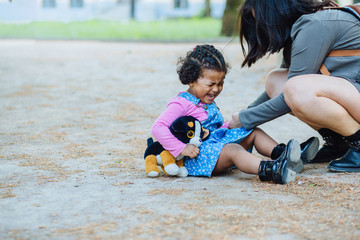 Disconsolate hispanic toddler girl three years old crying while sit on the ground outdoor. Her...