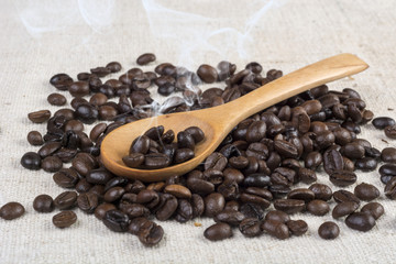 Fresh roasted coffee beans in wooden spoon smoke on retro desk. Aroma coffee concept. Close up, selective focus