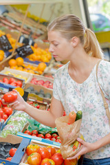Lady buying vegetables, holding a tomatoe