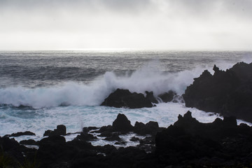 Waves crashing against black volcanic rock formations 