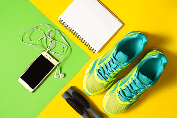 Sports equipment with shoes, skipping rope, blank notebook and mobile cellphone with earphones on colorful background. Top view, flat lay. Sport, fitness concept, healthy lifestyle