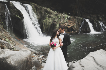 Beautifull wedding couple kissing and embracing near the shore of a mountain river with stones