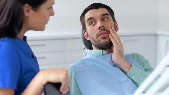 medicine, dentistry and healthcare concept - female dentist talking to male patient complaining of toothache at dental clinic office