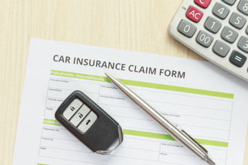 Top view of car insurance claim form with car key and calculator on wooden desk