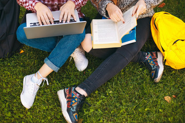 Students typing on a laptop and pointing with finger in a book 