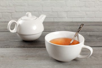 Fototapeta na wymiar White ceramic teapot and cup of hot amber tea on gray wood desk.