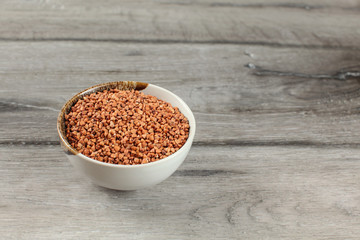 Small bowl full of buckwheat placed on gray wood desk.