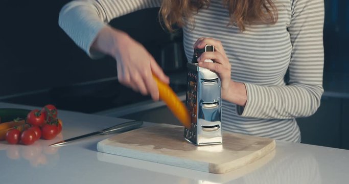 Young woman grating carrots in her kitchen