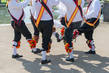 group of morris dancers wearing sashes and bells dance in a circle - obrazy, fototapety, plakaty