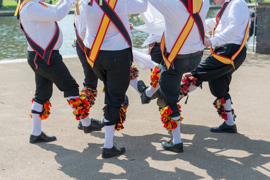 group of morris dancers wearing sashes and bells dance in a circle