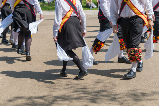 Group of male and female morris dancers wearing bells and white shirts and stockings dance on May Day Bank Holiday with sticks and handkerchiefs