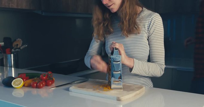 Woman grating carrots with boyfriend in background