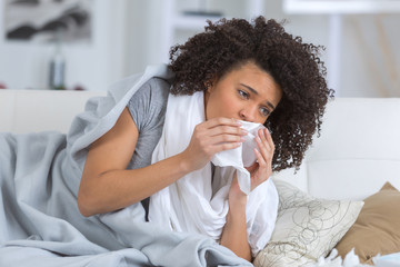 woman suffering from cold lying in bed with tissue