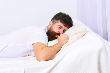 Man in shirt laying on bed, white wall on background. Nap and siesta concept. Macho with beard and...