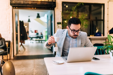 Shocked man in eyeglasses reading news on laptop while drinking coffee. Making a face.