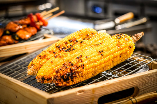 grilled corn on the grill with blur BBQ beside.