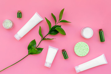 Fototapeta na wymiar Cosmetics for skin care with natural ingredients. Eco cosmetics. Cream, lotion, oil, tonic near young green leaves on pink background top view