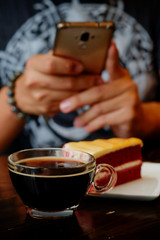 Fototapeta na wymiar taking photo with black coffee and red velvet cake on dark wooden table with smartphone with man hand. for up to social network .