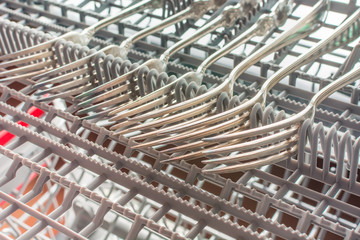 Silver forks lie in the upper compartment of the dishwasher