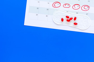 Menstruation cycle concept. Menstruation calendar with sanitary pads, contraceptive pills on blue background top view copy space