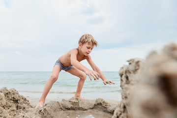 Fototapeta na wymiar Cute little boy building with sand on the background of sea
