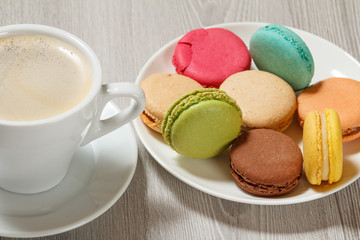 Cup of coffee and delicious macarons cakes of different color on white porcelain plate