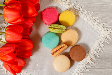 Sweet macarons cakes of different color on silk napkin with bouquet of red tulips