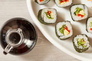 Sushi rolls with rice, pieces of avocado, cucumber and lettuce leaves on ceramic plate, glass bottle with soy sauce