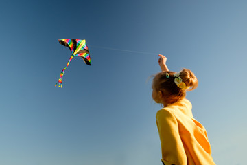 girl in yellow jacket plays with kite, blue clear sky background