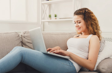 Obraz premium Young girl with laptop sitting on beige couch