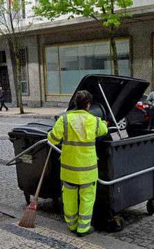 Woman of the municipal cleaning service overturning the urban trash bins in the container