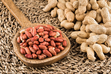 Peeled peanuts in a wooden ladle and peanuts in nutshell on natural matting