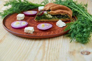 A piece of spinach pie with feta cheese, onion on the wooden table with free copy space. Decorated with fresh dill, onion rings and sliced feta. Vegetarian pie side view