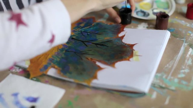 close-up, women's hands paints a picture on a maple leaf