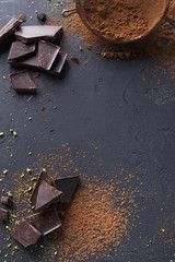 Dark chocolate pieces and cocoa powder over black background