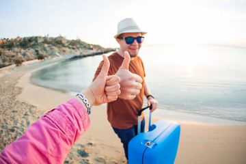 Young man arriving at the resort and standing on the beach while showing thumbs up