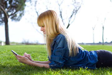 Pretty young woman using her mobile phone while lying on grass in the park.