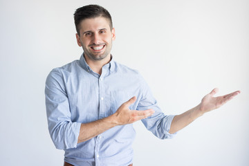 Portrait of cheerful young Caucasian manager showing product. Businessman wearing blue shirt pointing at something and smiling. Advertising concept