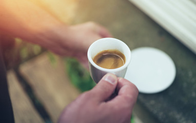 Male hand holding cup of espresso on terrace in the morning
