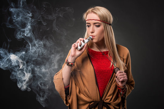 Portrait of sexy young hipster smoking vaping girl. The woman is dressed in the style of a boho. Vapor concept. Vaping e-Cigarette.