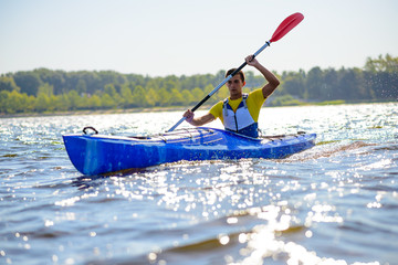 Young Professional Kayaker Paddling Kayak on River under Bright Morning Sun. Sport and Active Lifestyle Concept