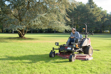 gardener cutting grass of a garden on a lawn mower