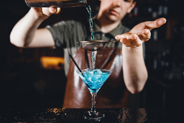 Barman mixes an alcoholic cocktail of blue color behind bar rack