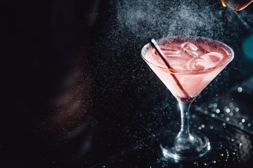 Large cocktail in martini glass with droplets of spray is prepared by barman.