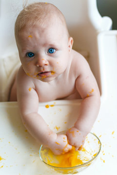 Beautiful baby eating her dinner and making a mess on his face and table. Baby food. Close up. Copy space.